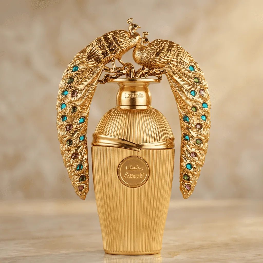 Perfume Afeef em frasco dourado canelado com tampa em formato de pavões cravejados de pedras coloridas, vista frontal sobre mármore
