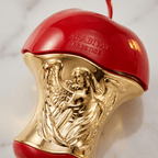 Detalhe em close-up do corpo dourado esculpido com anjo do frasco Forbidden da Arabiyat Prestige, em formato de maçã vermelha.