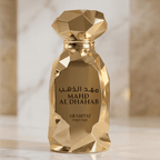 Perfume Mahd Al Dhahab da Arabiyat Prestige em close do frasco dourado facetado, com colunas de mármore ao fundo.