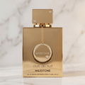 Perfume Club de Nuit Milestone da Armaf em frasco dourado com pingente, sobre fundo de mármore claro.