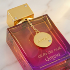 Perfume Club de Nuit Untold da Armaf em frasco degradê rosa e vermelho, com pingente dourado preso à tampa.