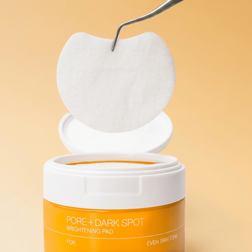 Pinça retirando um disco esfoliante do pote de Pore + Dark Spot Brightening Pad da Celimax, sobre fundo laranja.