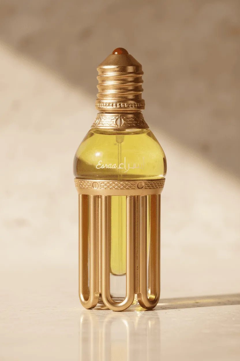 Óleo perfumado Esraa em frasco no formato de lâmpada com base dourada estriada, líquido amarelo dourado, sobre superfície de pedra clara