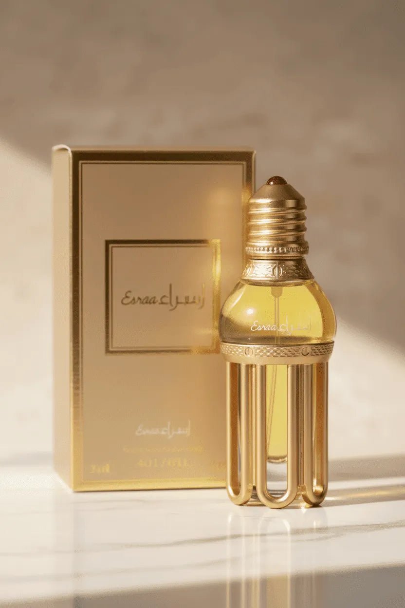 Óleo perfumado Esraa em frasco no formato de lâmpada dourada, ao lado da caixa original, com luz solar sobre mármore