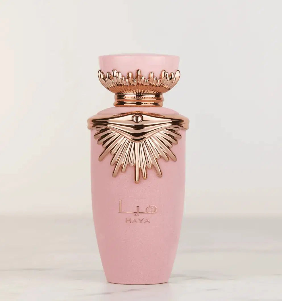 Perfume Haya em frasco rosa fosco com tampa dourada em formato de raios, fundo neutro
