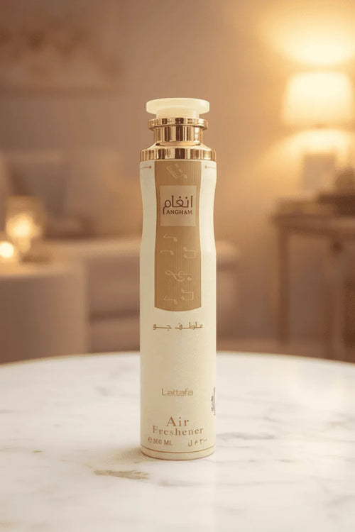 Air freshener Angham da Lattafa em frasco bege com tampa dourada, sobre mesa de mármore com ambiente aconchegante ao fundo