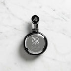 Perfume Fakhar Black da Lattafa em frasco redondo preto com medalhão prateado, fotografado de cima sobre mármore