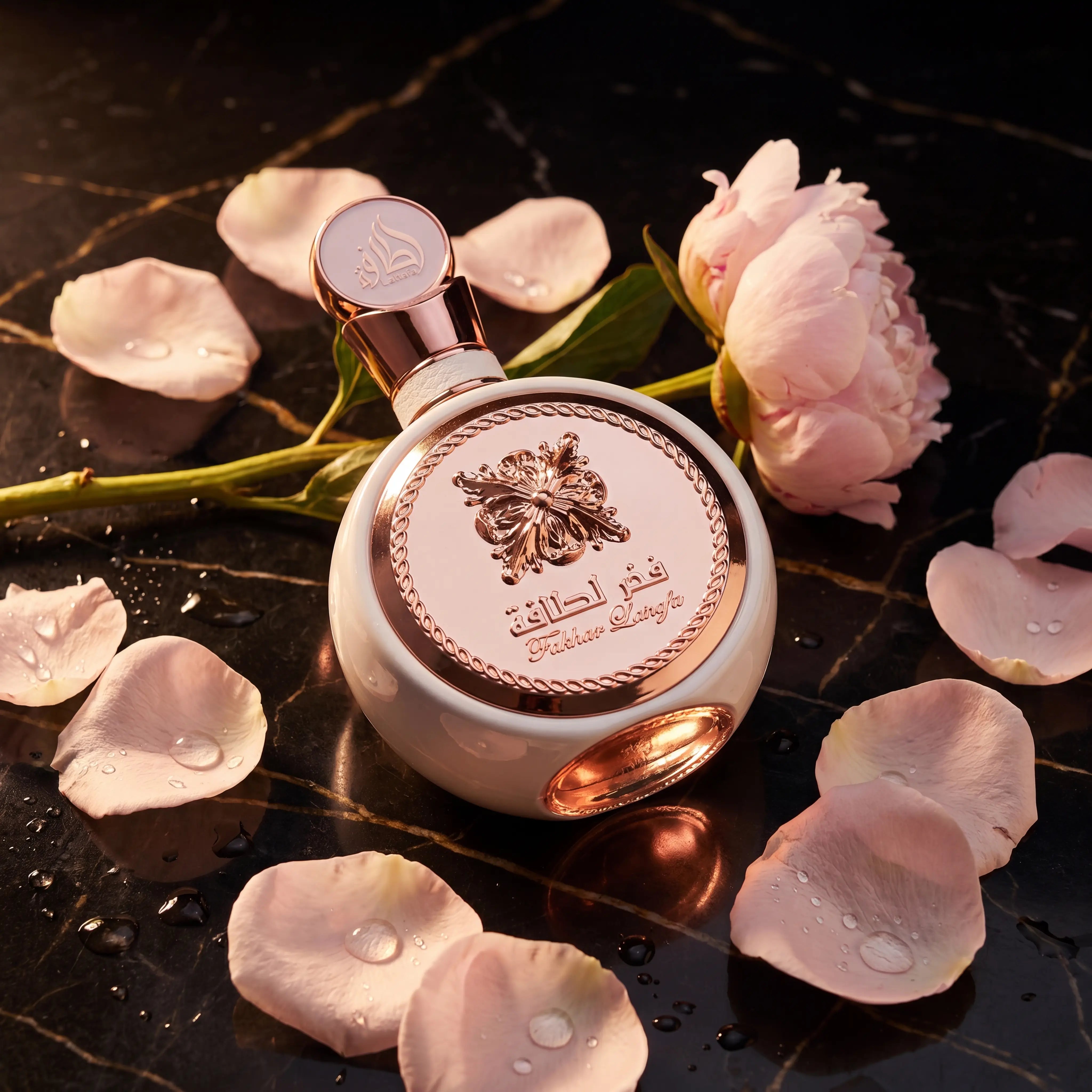 Perfume Fakhar Latifa da Lattafa em frasco redondo branco com detalhes rose gold, cercado por pétalas de flor rosa sobre mármore escuro.