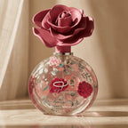 Perfume Layaan da Lattafa em frasco redondo pintado com flores rosa, tampa em formato de rosa, ao fundo cortina bege
