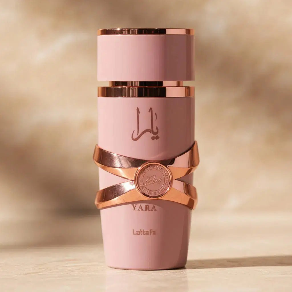 Perfume Yara da Lattafa em frasco rosa com faixas rosé gold cruzadas, sobre fundo desfocado em tons dourados