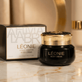 Creme corporal Léonie Ultimate Hydration, pote preto com tampa dourada ao lado da caixa, 100ml.