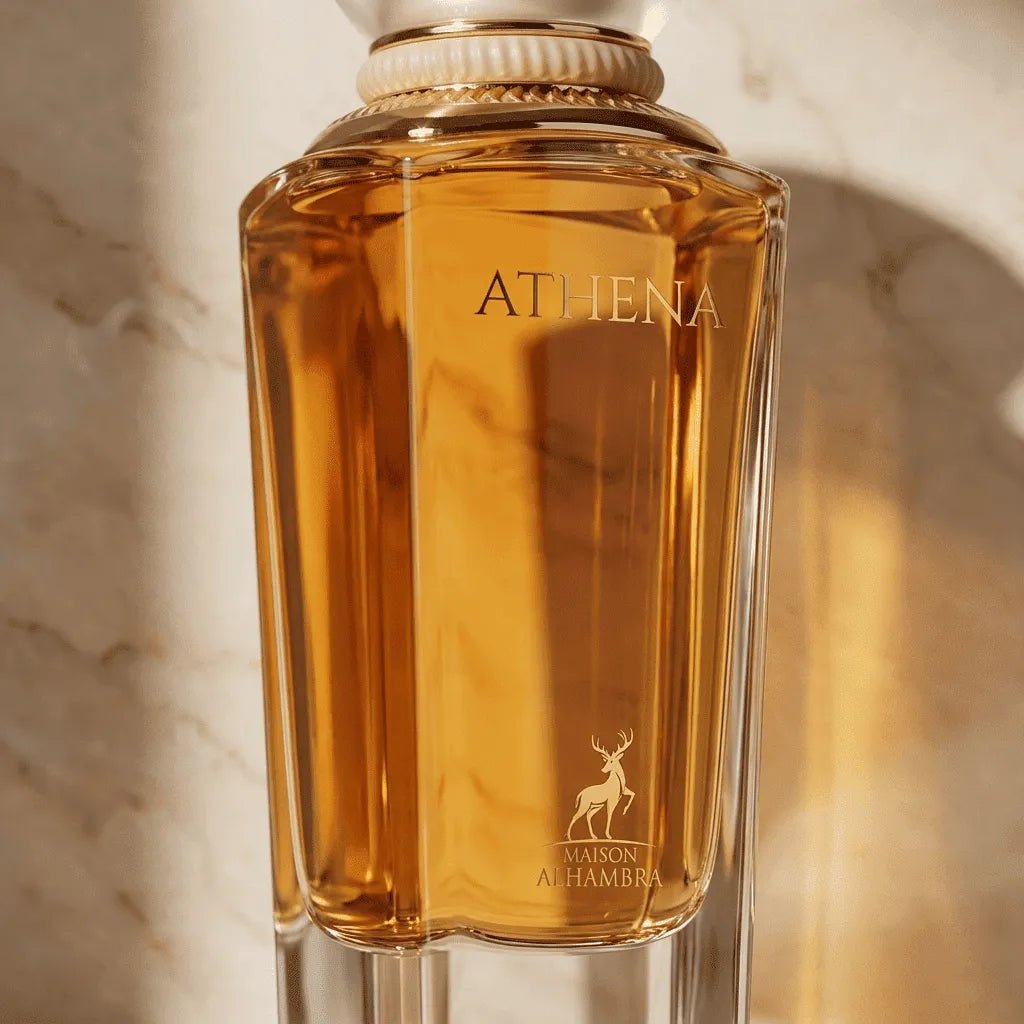 Close-up do frasco facetado do perfume Athena da Maison Alhambra, líquido âmbar iluminado por luz natural sobre mármore