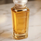 Perfume Athena da Maison Alhambra em frasco facetado âmbar com tampa perolada e detalhes dourados, sobre mármore