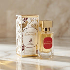 Perfume La Rouge Baroque da Maison Alhambra em frasco dourado com rótulo vermelho, ao lado da caixa branca com estampa dourada, sobre mármore em tom quente