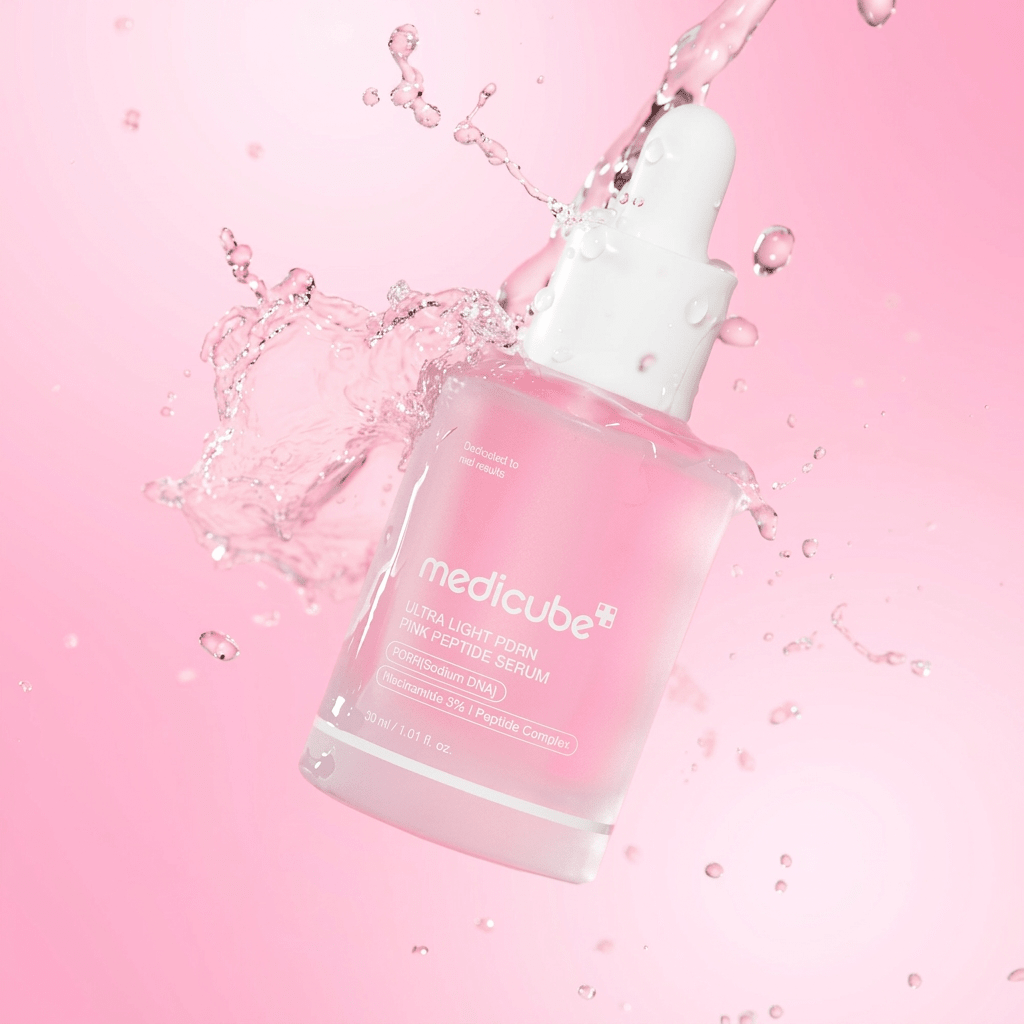 Sérum Ultra Light PDRN Pink Peptide Serum da Medicube com respingos de líquido rosa ao redor do frasco, fundo rosa vibrante.
