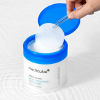 Pinça retirando um disco esfoliante Zero Pore Pad do pote da Medicube, com respingos de água ao fundo.