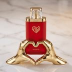 Perfume Nusuk em frasco vermelho, apoiado sobre suporte dourado em formato de mãos fazendo coração.