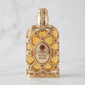 Perfume Exclusive Royal Amber da Orientica em frasco dourado ornamentado, sobre mármore branco.
