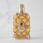 Perfume Exclusive Royal Amber da Orientica em frasco dourado ornamentado, sobre mármore branco.