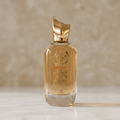 Frasco do perfume Ameerati em dourado com tampa em formato de chama, sobre superfície de mármore