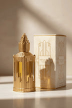 Perfume em frasco dourado com design art déco, ao lado da caixa creme e dourada original, com luz solar e sombras