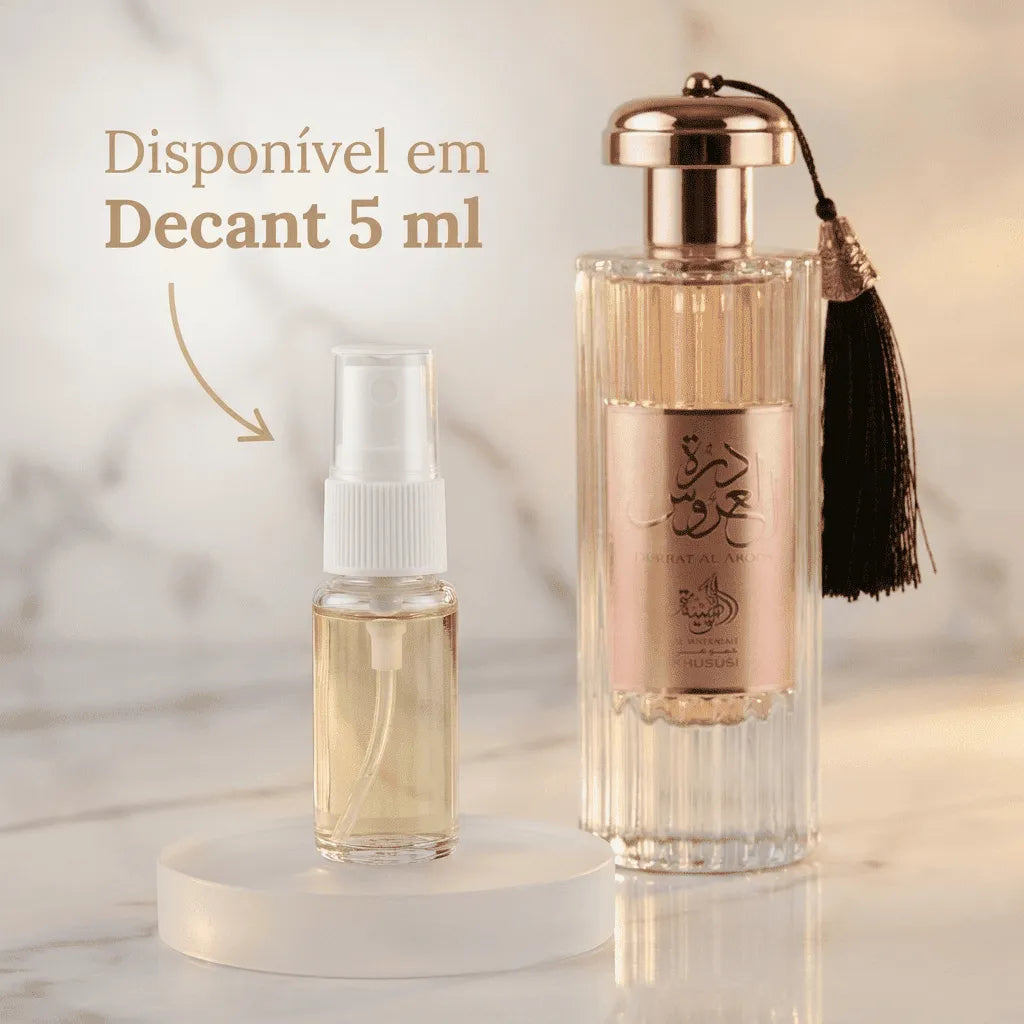 Perfume Durrat Al Aroos em frasco transparente estriado com tampa rosé gold e borla preta, ao lado de decant de 5ml