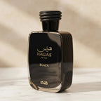 Perfume Hawas Black da Rasasi, frasco preto com tampa trançada, ângulo lateral sobre mármore claro.