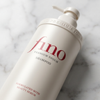 Frasco bege do shampoo Fino Premium Touch deitado sobre superfície de mármore claro, em ângulo aproximado.